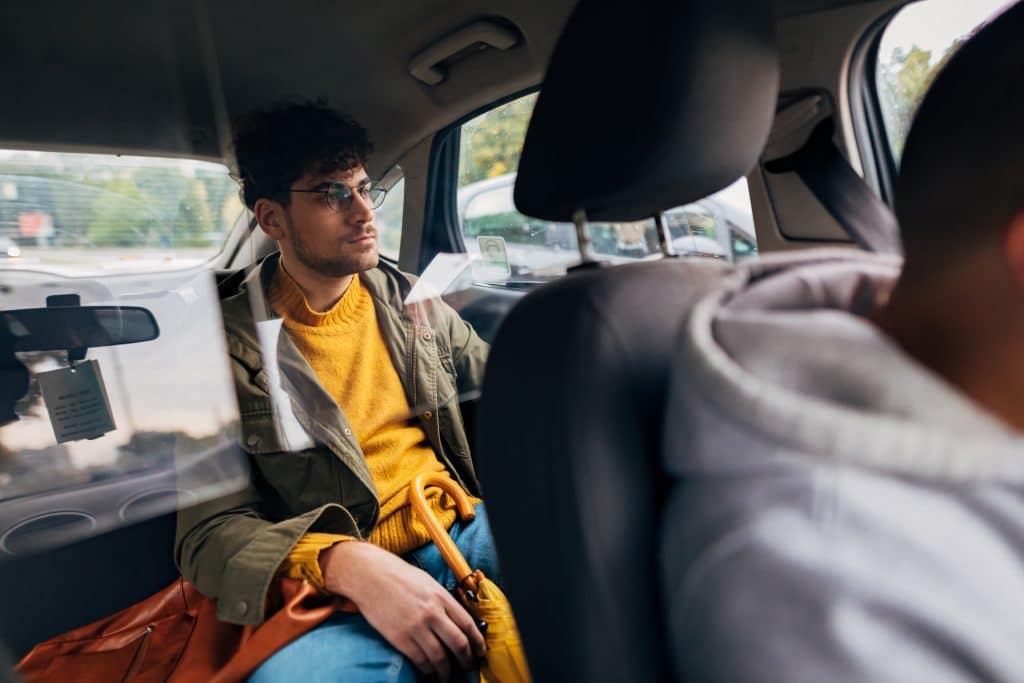 Passenger sitting in the back seat of a car, looking out the window while the driver focuses on the road.