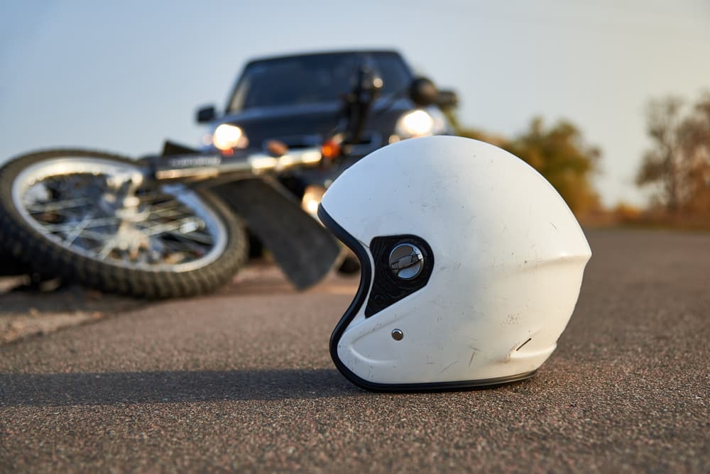 Motorcycle helmet on the ground with a fallen bike and car nearby.