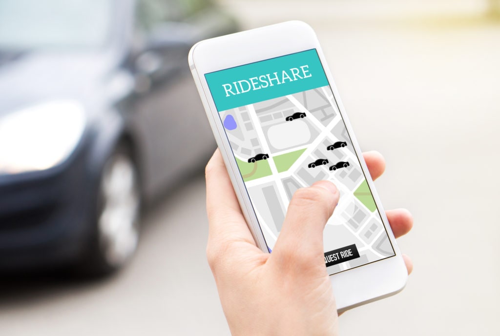 Person using a rideshare app on a smartphone with a car in the background, representing ride-hailing services like Uber or Lyft.