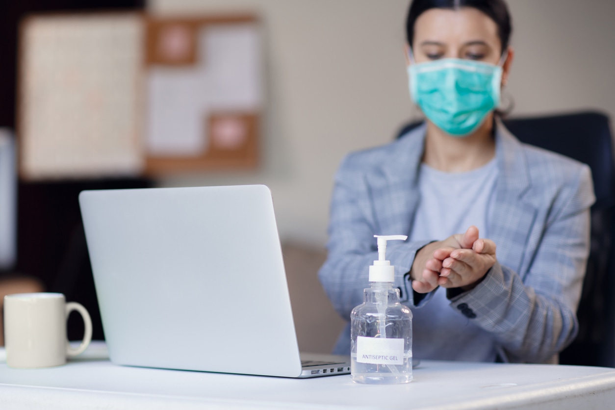 woman at the office wearing facemask and using hand sanitizer