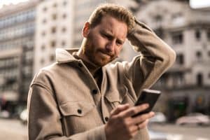 A man in Austin, Texas looks at his phone in confusion due to an insurance company intentionally delaying his claim.