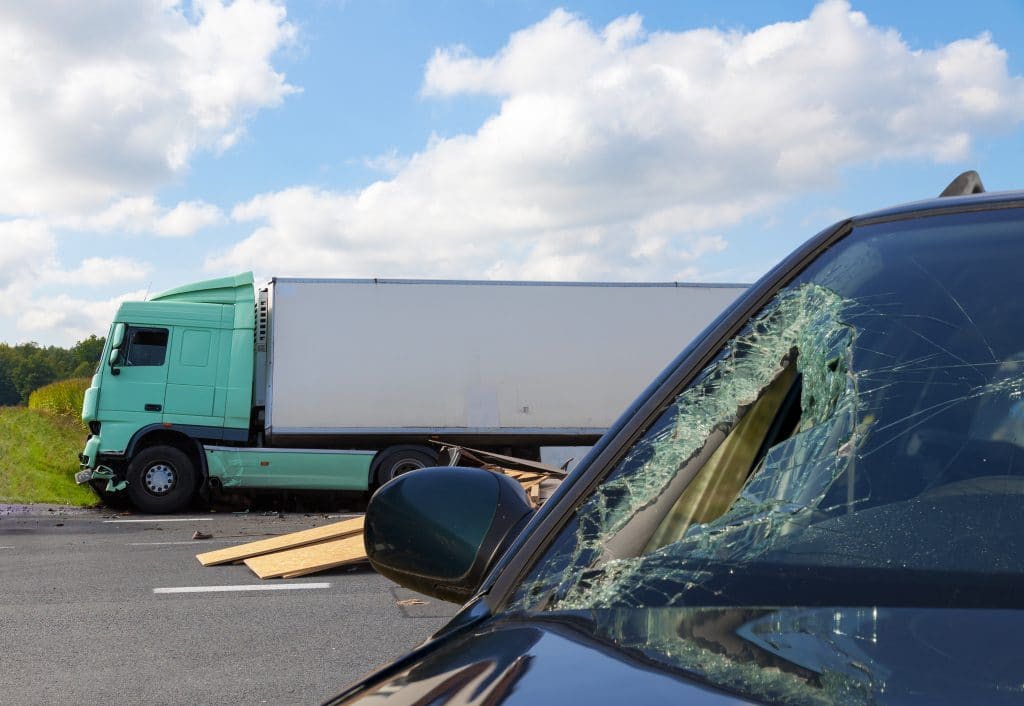 A damaged car after a truck crash with the semi truck in the background.