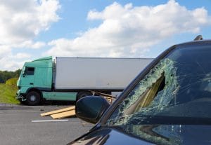 A damaged car after an accident with the semi truck in the background.