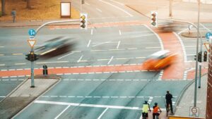 City crossroads aerial view with motion-blurred traffic, including cars and cyclists on the bike path, creating a dynamic urban intersection scene.