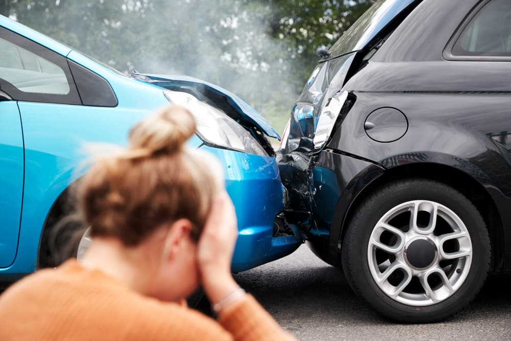 Upset woman sitting next to vehicles involved in a car accident, holding her head in despair.