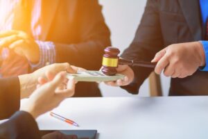 Exchange of settlement money between two individuals with a judge's gavel in the foreground, representing the success of legal advocacy.