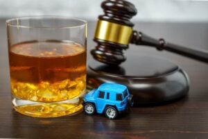 Whiskey glass with ice near a gavel and a toy car, implying legal consequences for DWI.