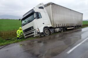 A truck has slipped off a slick road into a field, and a person is looking it over.