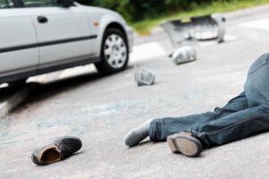 A pedestrian lies on the road with scattered belongings after a car accident.