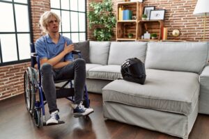 Young man in wheelchair after motorcycle accident, displaying skepticism and nervousness, arms crossed with a disapproving expression – conveying a negative attitude.