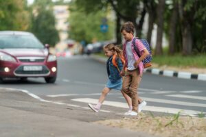Young girl and boy with backpacks safely cross the road at a pedestrian crossing on their way to school. Prioritizing pedestrian safety.