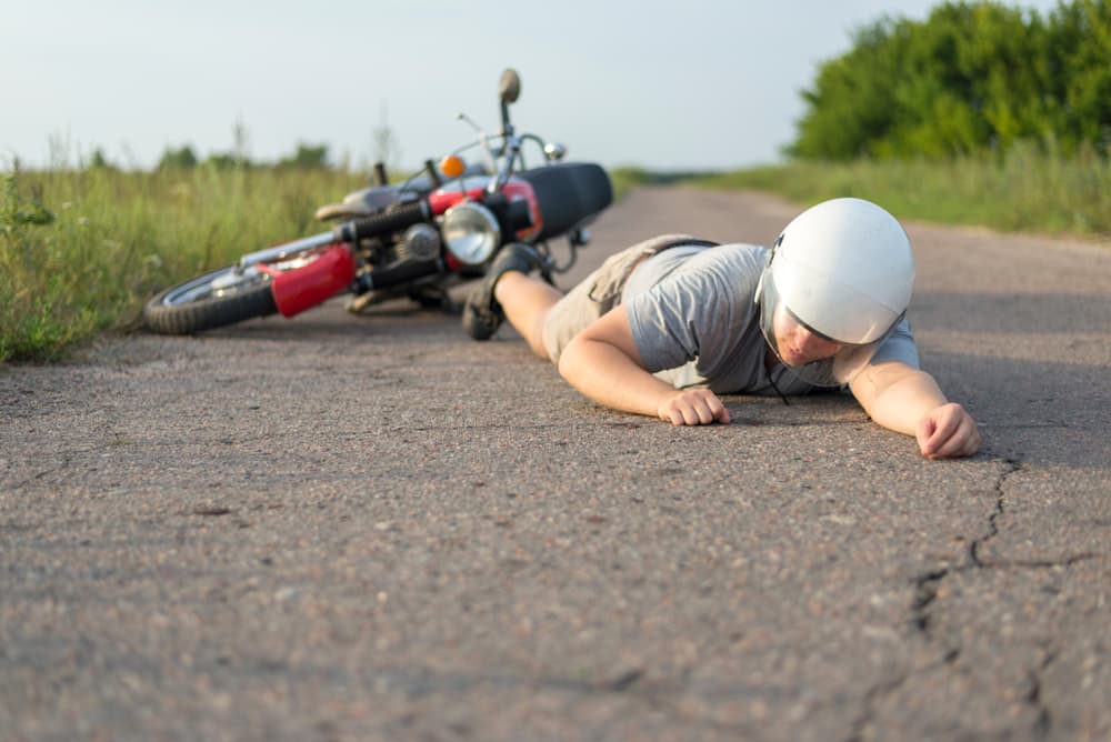 A man lies beside his motorcycle on the asphalt, illustrating the theme of road accidents.