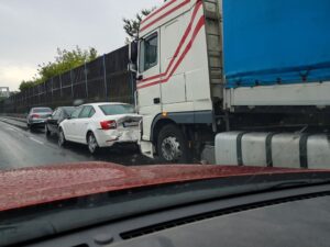 A damaged car after a collision with a truck on a wet road, viewed from another vehicle's perspective.