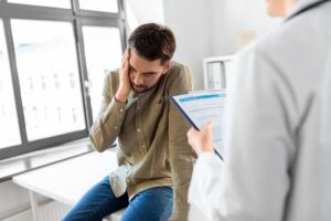 Healthcare scene: Female doctor with clipboard addresses a sad male patient with health issues in a hospital.