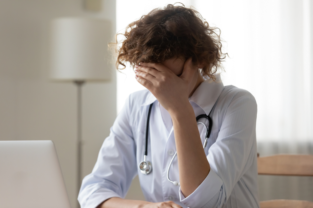 Young woman doctor covering face with hand, feeling desperate and guilty after a death of her patient