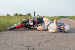 A man lies on the asphalt near his motorcycle, depicting the theme of road accidents and their consequences.
