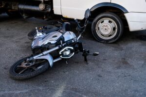 Silver motorcycle on city street asphalt after collision with cargo vehicles.