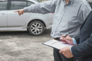 Loss adjuster inspects damaged car while a sales manager advises on application documents for a car insurance mortgage loan offer.