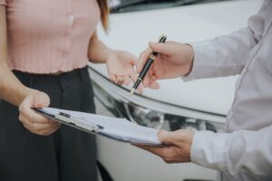 An insurance agent inspects a damaged car and fills out a report claim form after an accident. Illustrates traffic accident and insurance concept.
