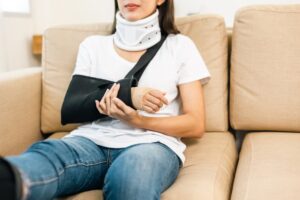 Woman recovering from car accident with leg, neck, and arm support in living room. Health insurance and rehabilitation concept.