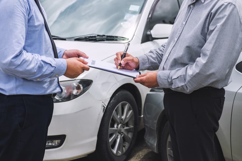 Insurance agent inspects damaged car as customer signs claim report form after accident. Traffic accident and insurance concept. Insurance agent inspects damaged car as customer signs claim report form after accident. Traffic accident and insurance concept.