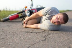 A man lies on the asphalt clutching his knee near his motorcycle, depicting a road accident scene.