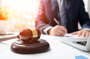 A wooden gavel rests on a table in a courtroom as an attorney works, symbolizing justice, law, and legal proceedings.