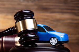 A gavel rests beside a blue car next to a law book on a wooden desk.
