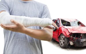 Close-up of a man with bandaged arm with a wrecked red car in the background.