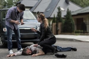 A woman assists a car accident victim while a man uses a cellphone to call for help.