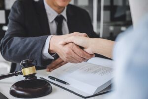 A woman shaking hands with a lawyer in a courtroom after discussing a contract deal.