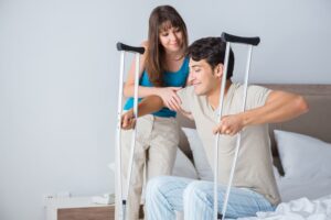 Young woman assisting her husband using crutches after an injury, showing support and care