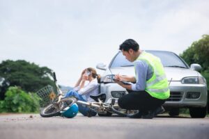Traffic officer investigates car and bicycle accident, injured cyclist in background.