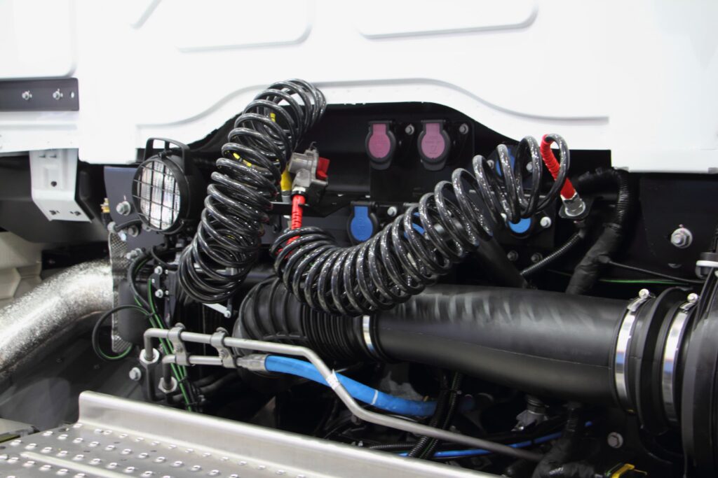 Close-up of commercial truck air brake and electrical connections with coiled air hoses and service couplings mounted behind the cab.