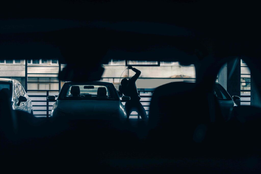 Silhouette of a car break-in suspect attempting vehicle theft inside a dimly lit parking garage. Silhouette of a car break-in suspect attempting vehicle theft inside a dimly lit parking garage.