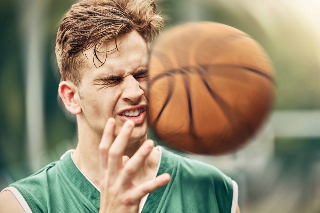 Basketball player hit in the face by a ball during an outdoor game, capturing a sports injury moment. Basketball player hit in the face by a ball during an outdoor game, capturing a sports injury moment.