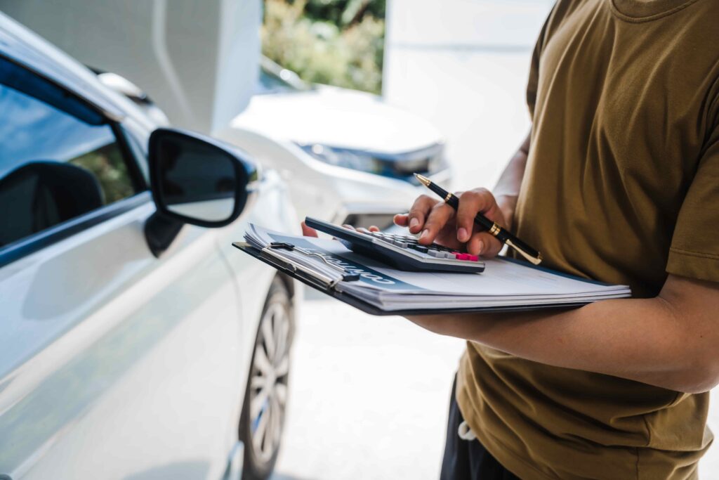 Auto insurance adjuster calculating repair estimate on clipboard next to a car for vehicle damage claim. Auto insurance adjuster calculating repair estimate on clipboard next to a car for vehicle damage claim.