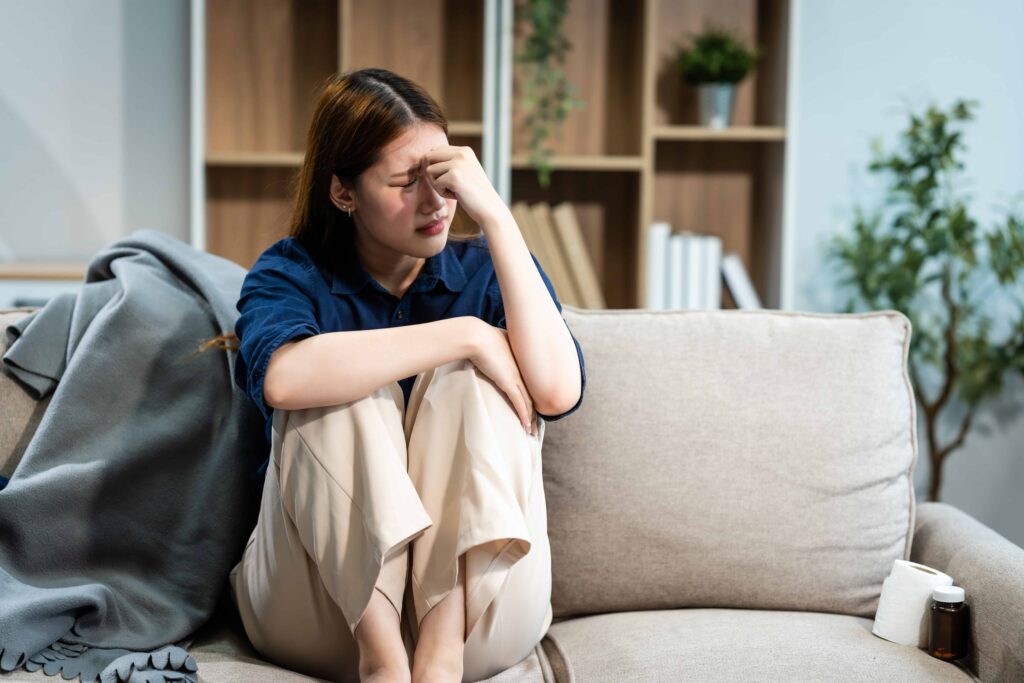 Young woman sitting on a sofa holding her head in pain, showing stress, headache, or emotional distress at home. Young woman sitting on a sofa holding her head in pain, showing stress, headache, or emotional distress at home.