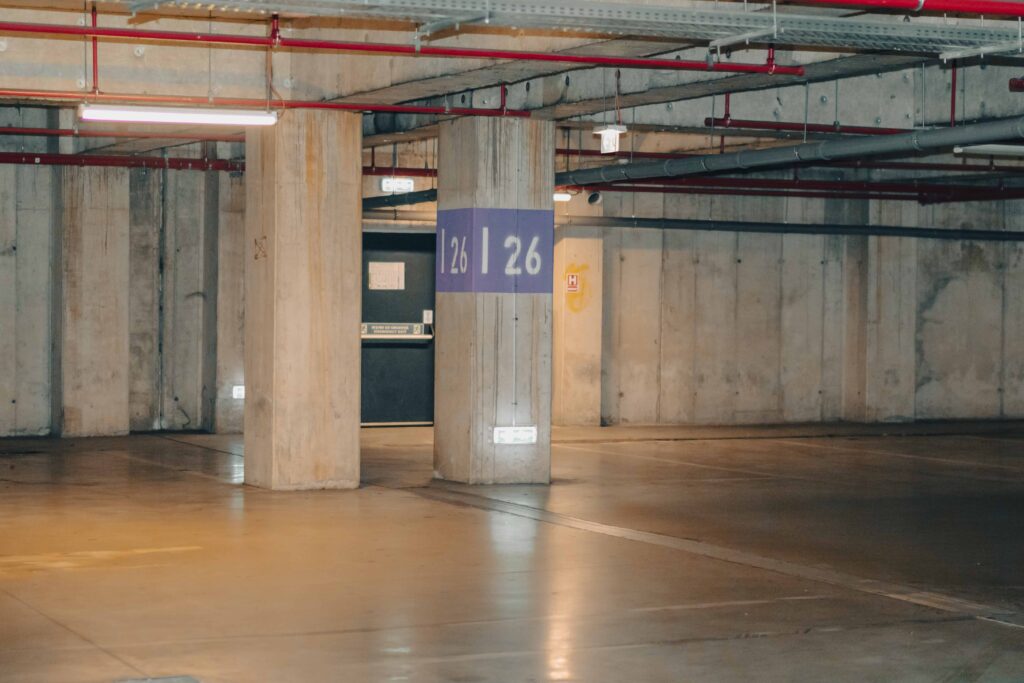 Empty underground parking garage with concrete pillars, numbered parking section signs, and industrial lighting. Empty underground parking garage with concrete pillars, numbered parking section signs, and industrial lighting.