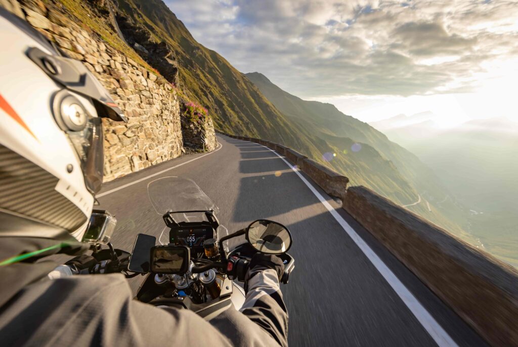 POV of a motorcyclist riding on a winding mountain road at sunset, with scenic valley views and stone guardrail. POV of a motorcyclist riding on a winding mountain road at sunset, with scenic valley views and stone guardrail.